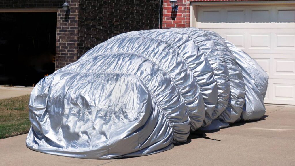 Car parked in driveway on sunny day with a silver car cover completely covering the car