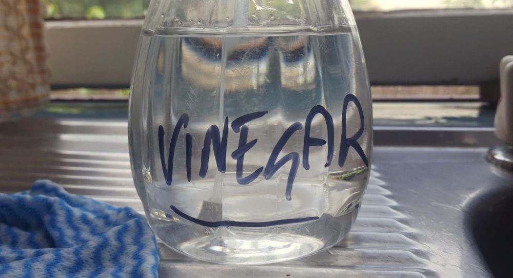 Base of a clear spray bottle with clear liquid inside. Words vinegar written with sharpie on it.